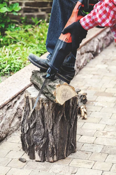 Man in plaid shirt sawing piece of wood on stump — Stock Photo, Image