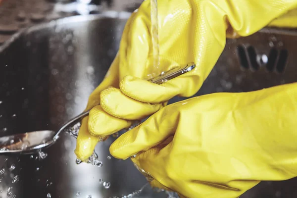 Hands in yellow rubber gloves, wash spoon in sink