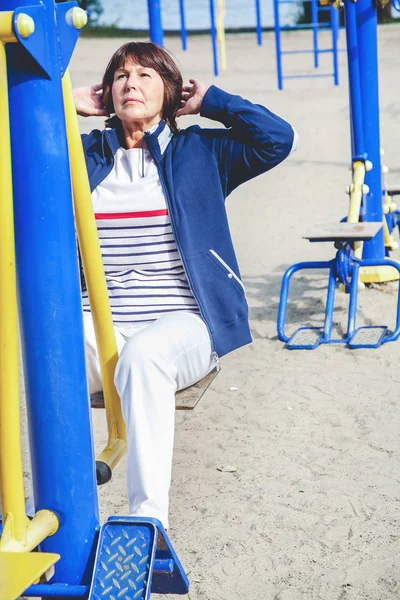 Пожилая женщина занимается спортом на уличном тренажере — стоковое фото