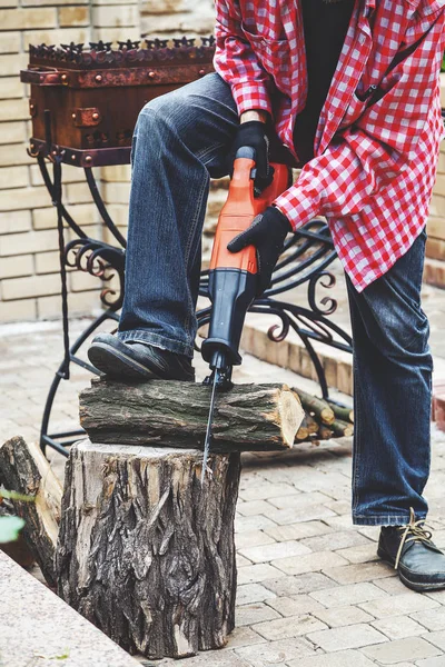 Man in plaid shirt sawing piece of wood on stump — Stock Photo, Image