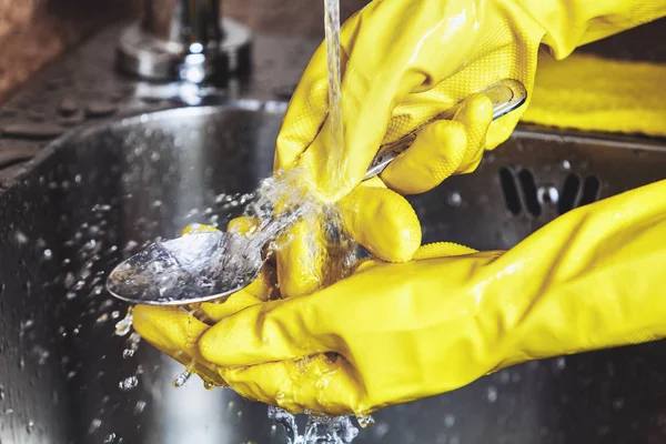 Manos en guantes de goma amarillos, lavar la cuchara en el fregadero — Foto de Stock