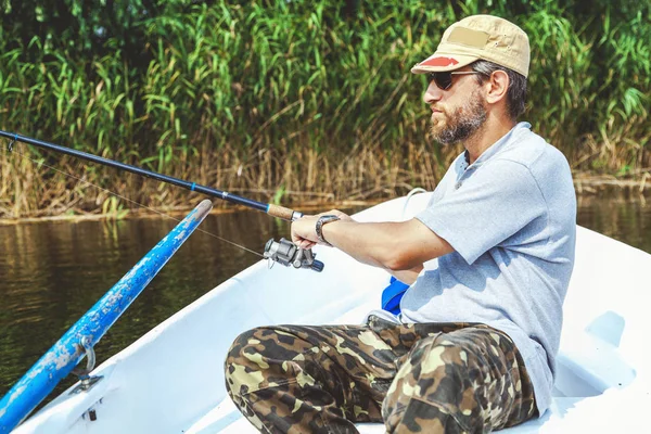 Pescador con barba sentado en barco y sosteniendo caña de pescar —  Fotos de Stock