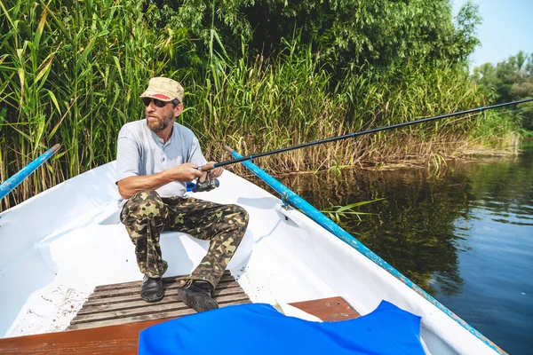 Fisherman with beard sitting in boat and holding fishing rod — Stock Photo, Image