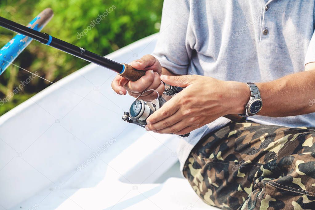 Hands fisherman holding fishing rod and reel handle is rotated