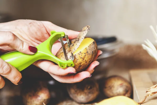 Очищення картоплі. руки жінки очищають картоплю зі спеціальною т — стокове фото