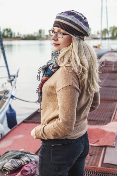 Bonita rubia en un suéter y tomar posiciones en el muelle —  Fotos de Stock