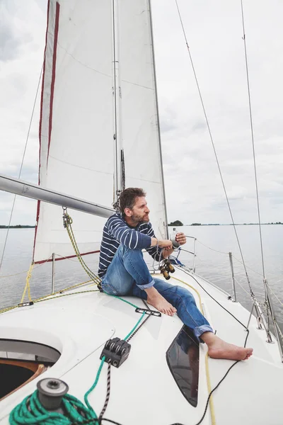 Man in striped sweater sits on white sailing yacht — Stock Photo, Image