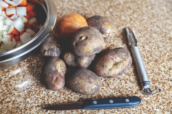 Několik brambor a nůž leží na mramorové desce — Stock fotografie