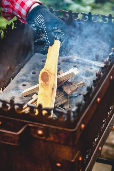 Рука кладет крошечные чипсы в огонь жаровни близко — стоковое фото
