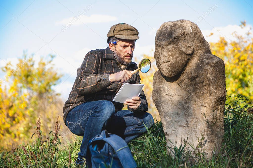 Scientific historian examines through magnifying glass stone scu