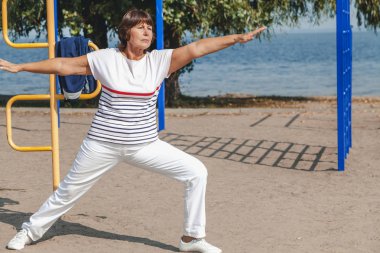 Jimnastik sahilde. emekli kadın egzersizleri kumlu g üzerinde gerçekleştirir.
