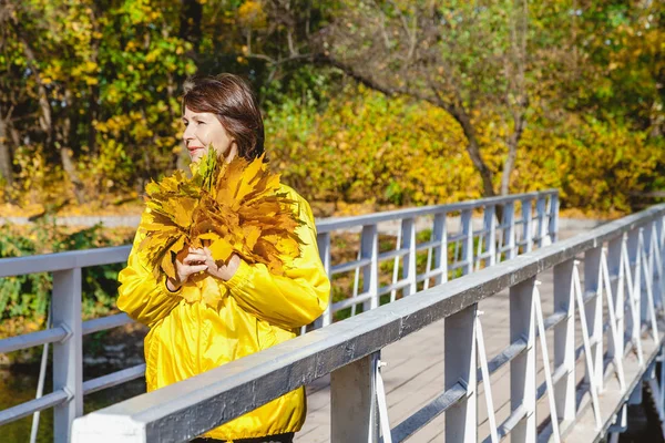 Beautiful older woman standing on bridge with bunch of leaves — Stock Photo, Image