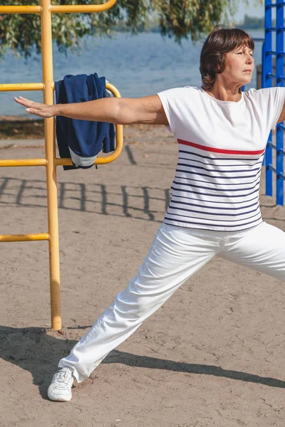 Jimnastik sahilde. emekli kadın egzersizleri kumlu g üzerinde gerçekleştirir.