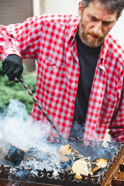Человек превращает дрова в горящую жаровню с кованой кочергой — стоковое фото