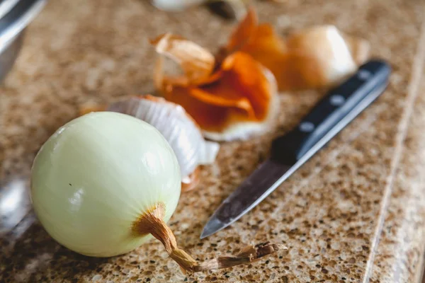 Bombilla pelada de cáscara de cebolla y cuchillo sobre mesa de mármol — Foto de Stock