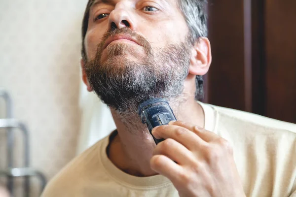 Grooming beard. man is cutting a beard in the bathroom