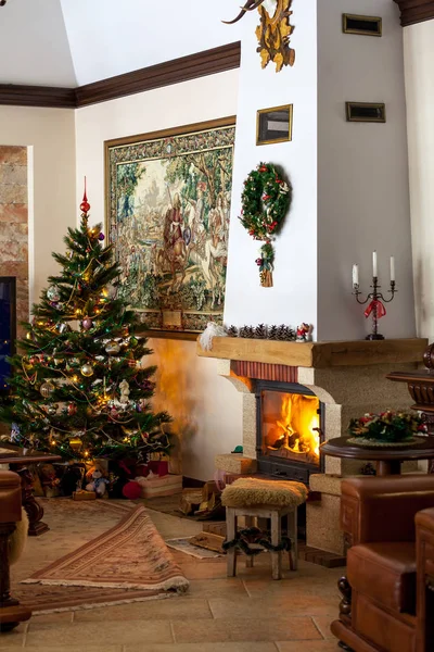 Cozy New Year atmosphere in a luxurious castle. A decorated Christmas tree stands in the corner of the fireplace hall of a large hous
