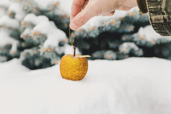 Рука аккуратно кладет на снежную игрушку золотое яблоко — стоковое фото