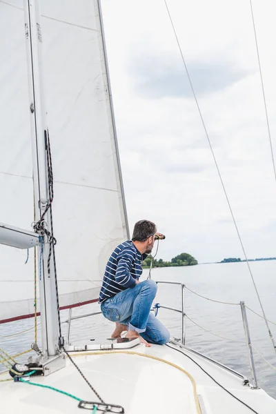 Man sits on sailing yacht and looks through binoculars — Stock Photo, Image