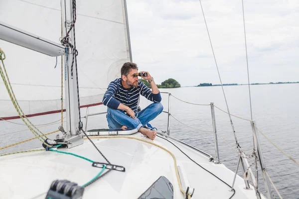 Man sits on sailing yacht and looks through binoculars — Stock Photo, Image