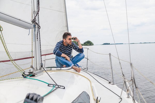 man sits on sailing yacht and looks through binoculars