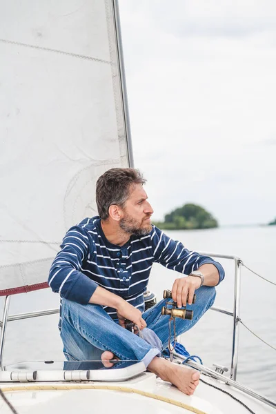 Мужчина сидит в носовой части парусной яхты и смотрит за борт — стоковое фото