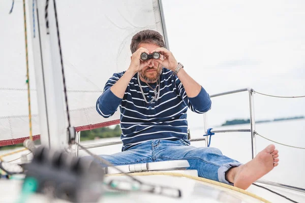 Человек сидит на парусной яхте и смотрит в бинокль — стоковое фото