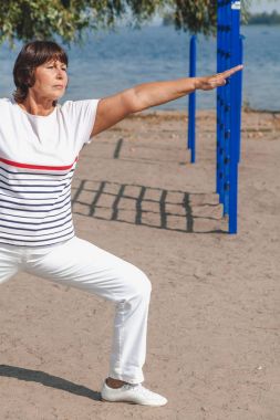 Jimnastik sahilde. emekli kadın egzersizleri kumlu g üzerinde gerçekleştirir.