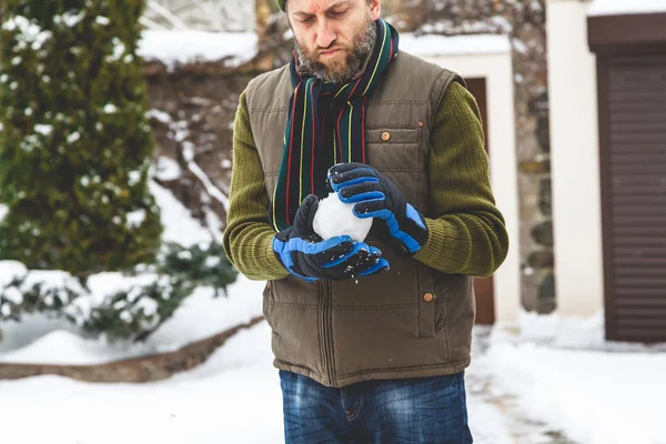 Человек с бородой делает снежок во дворе — стоковое фото