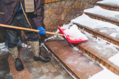 Lastik çizmeler erkekte tuğla merdiven ile büyük bir kırmızı plastik kıpırdamak adımlardan kar kaldırır