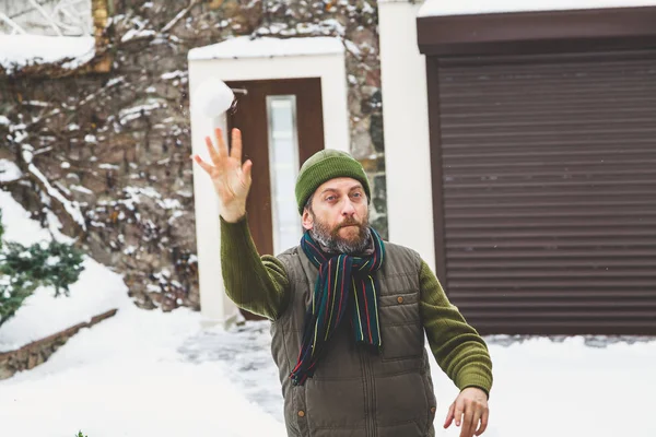 man with beard in his cap throws snowballs in yard