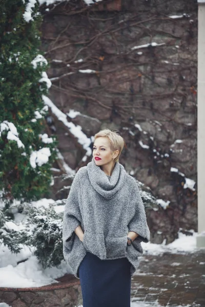 Leuke vrouw in grijze trui staat tegen de stenen muur — Stockfoto