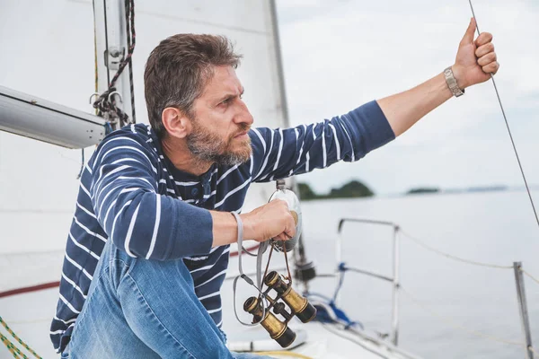 Людина з бородою сидить на палубі вітрильної яхти — стокове фото