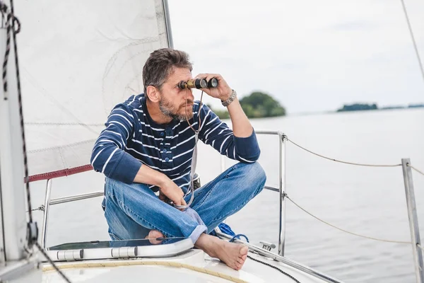 Людина сидить на вітрильній яхті і дивиться через бінокль — стокове фото