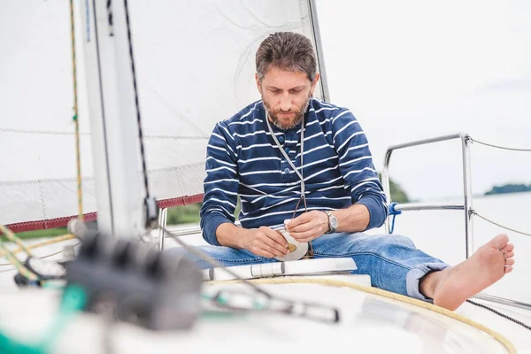 Man sits on bow of sailing yacht and holds jar — Stock Photo, Image