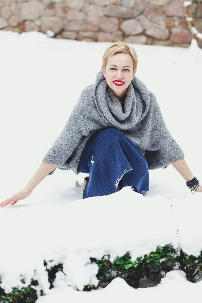 Hermosa mujer en suéter gris agachado en el patio cubierto de nieve —  Fotos de Stock