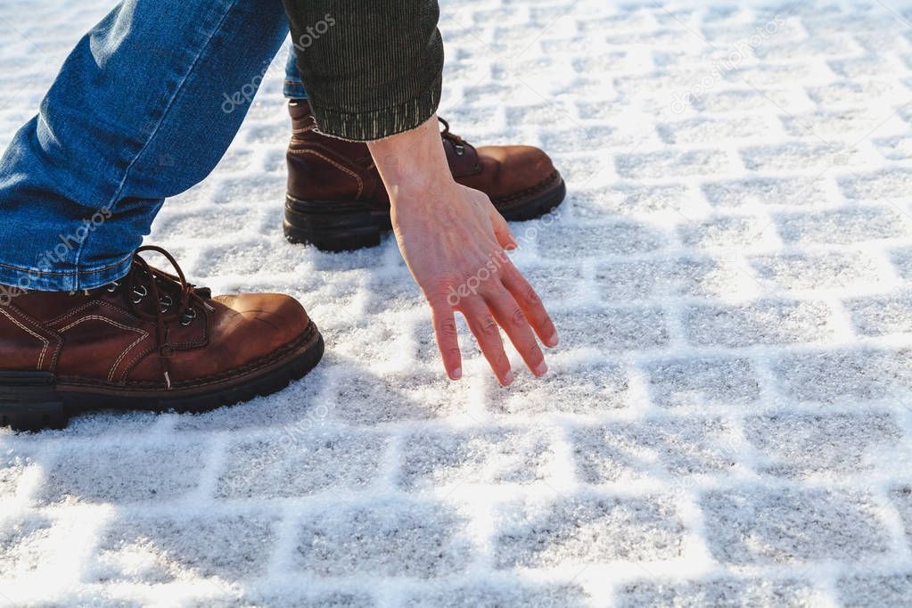 man in boots touches hoar frost on sidewalk tile