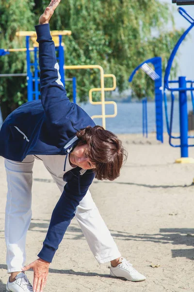 elderly woman performs sloping exercises on summer sports ground