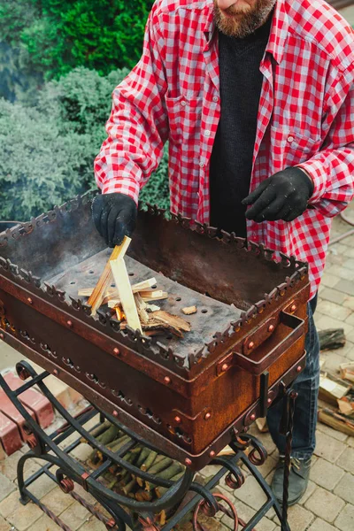 Человек в клетчатой рубашке кладет доски в огонь барбекю — стоковое фото