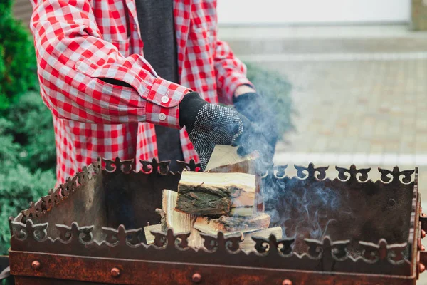 Человек в клетчатой рубашке кладет доски в огонь барбекю — стоковое фото