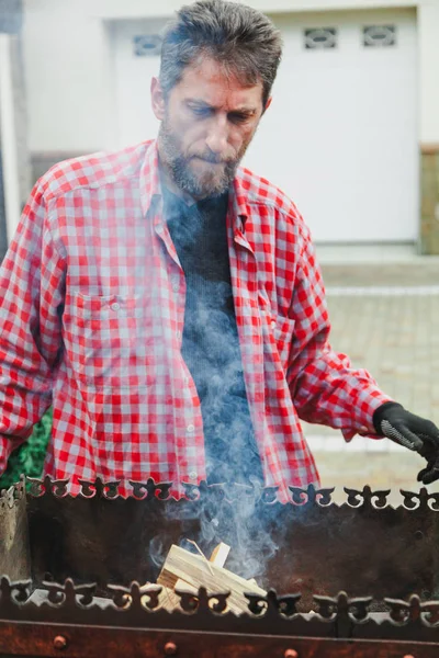 Человек с бородой кладет дрова в огонь мангала — стоковое фото