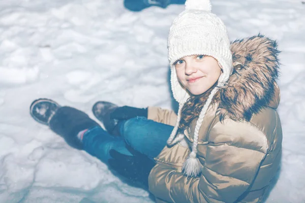 Jong meisje in witte hoed zitten in de sneeuw — Stockfoto