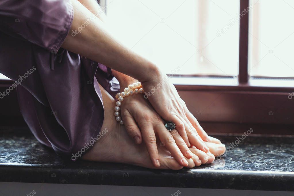 Bare feet of woman stand on granite window sill