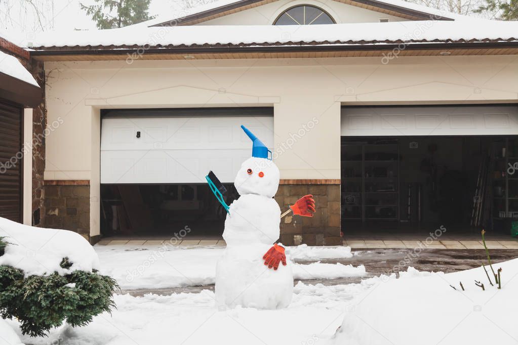 funny snowman stands in front of  garage