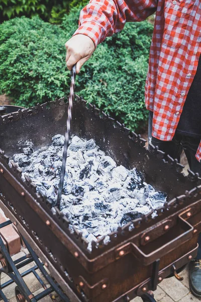 Man rakes coals in brazier with metal poker — Stock Photo, Image