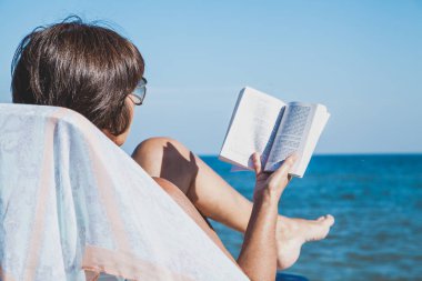 Yaşlı kadın plajda kitap okuma