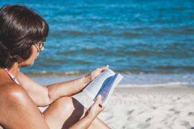 Yaşlı kadın plajda kitap okuma