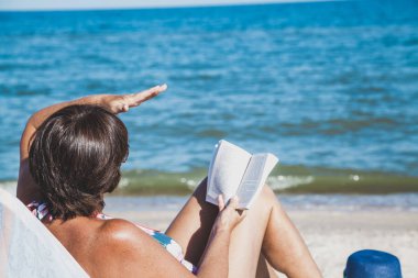 Yaşlı kadın plajda kitap okuma