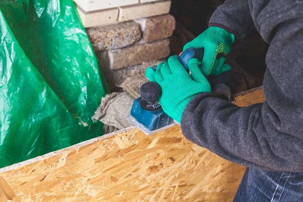 Manos en guantes planean la placa de madera con un plano eléctrico — Foto de Stock