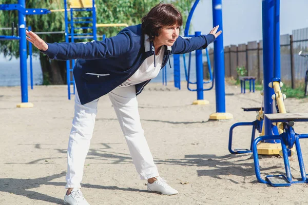 Пожилая женщина выполняет упражнения по наклону на летней спортивной площадке — стоковое фото